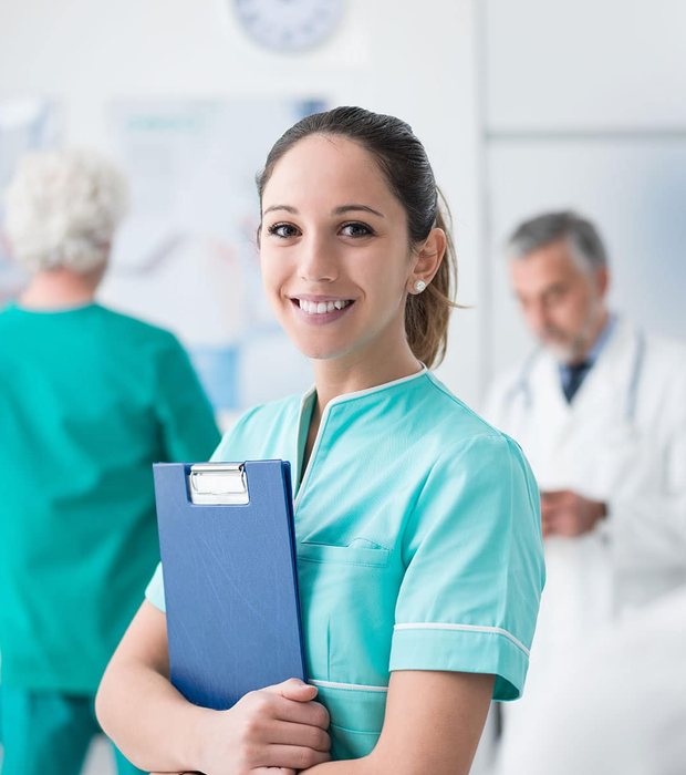 A smiling nurse holding a patient clipboard in the clinic